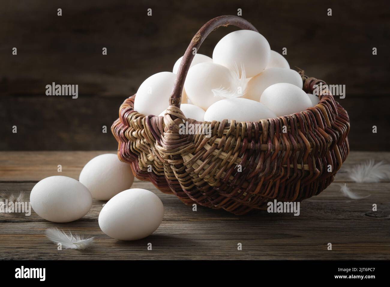 Panier en osier rempli d'œufs de poulet blancs sur une table en bois. Banque D'Images
