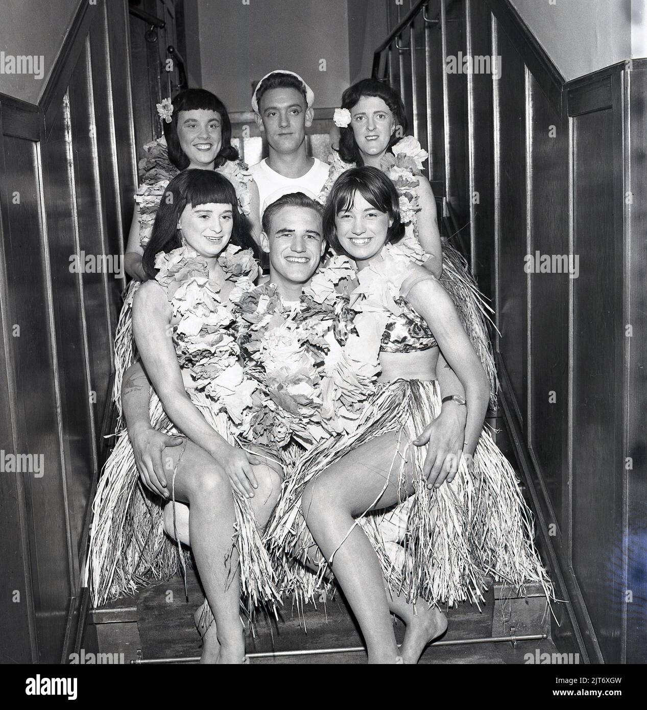 1965, historique, production théâtrale du Pacifique Sud, coulisses sur un escalier, les artistes se réunissent pour une photo de groupe, deux heureux 'ailors' avec des filles en jupes de gazon, Fife, Écosse, Royaume-Uni. South Pacific est une comédie musicale écrite par le partenariat à succès de Rodgers et Hammerstein, basée sur le livre Tales of the South Pacific et qui a été créée sur Broadway en 1949. Banque D'Images
