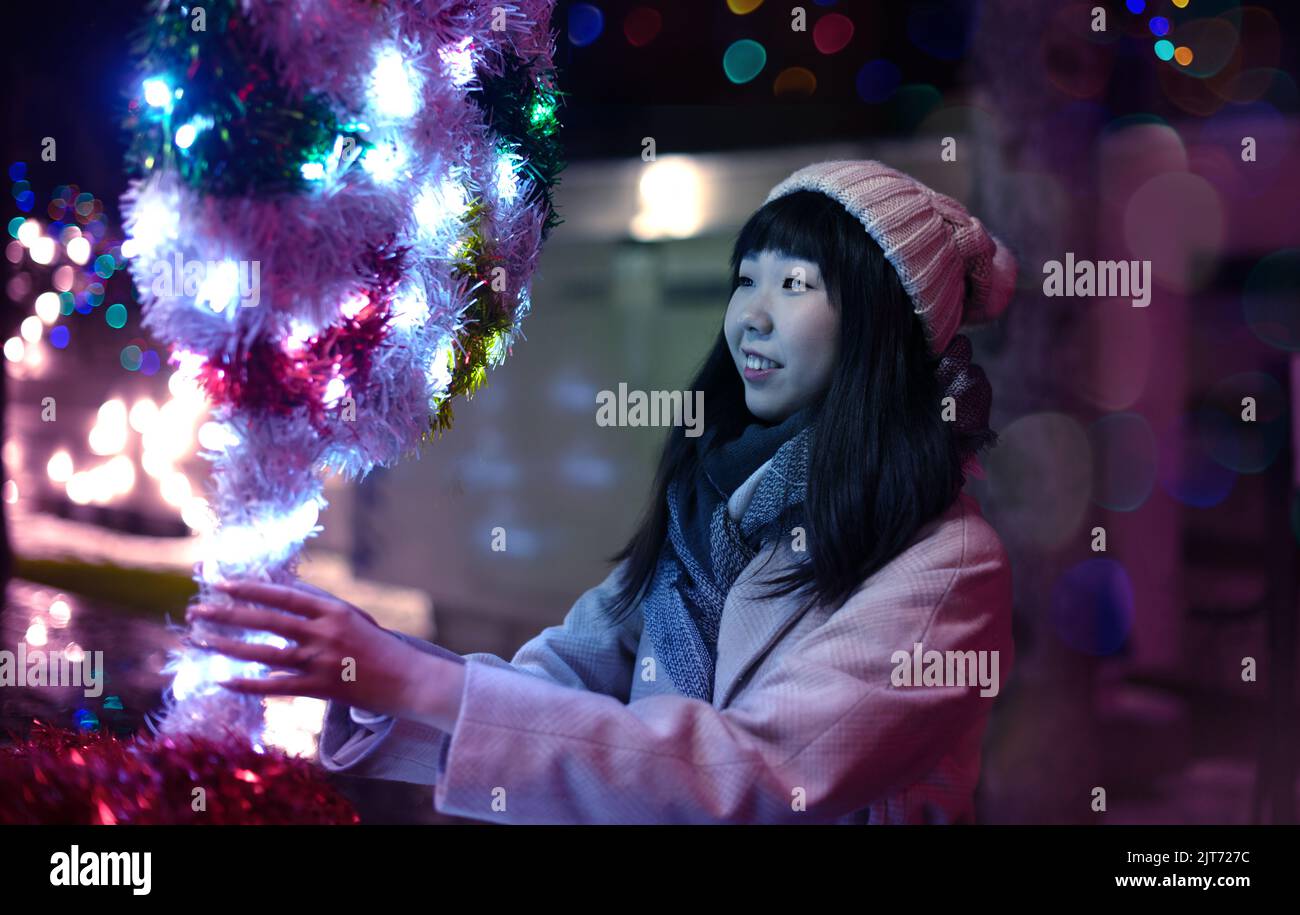 Une jeune femme coréenne à la mode dans un chapeau et un manteau marche dans les rues de Noël de la ville dans la soirée. Banque D'Images