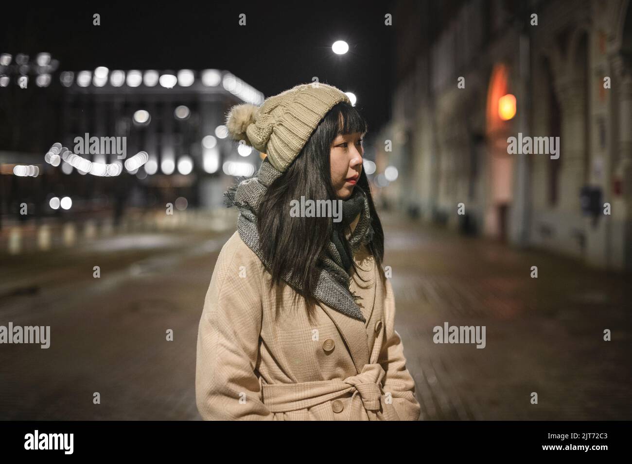 Une jeune femme coréenne à la mode dans un chapeau et un manteau marche dans les rues de Noël de la ville dans la soirée. Banque D'Images