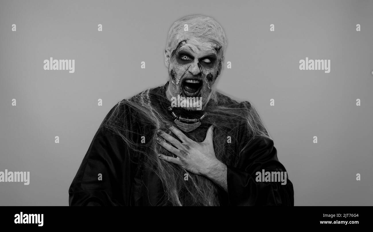 Sinistre homme en costume de carnaval de Halloween zombie fou avec sanglant blessé cicatrices visage pointant du doigt vers l'appareil photo, riant à voix haute, tauntant rendant amusant de l'apparence ridicule, drôle de blague. Horreur Banque D'Images