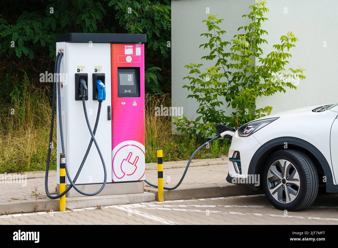 Une voiture électrique blanche branchée dans une station de charge pour charger leurs batteries dans un parking près de la rue. Véhicule électrique, multisegment Banque D'Images