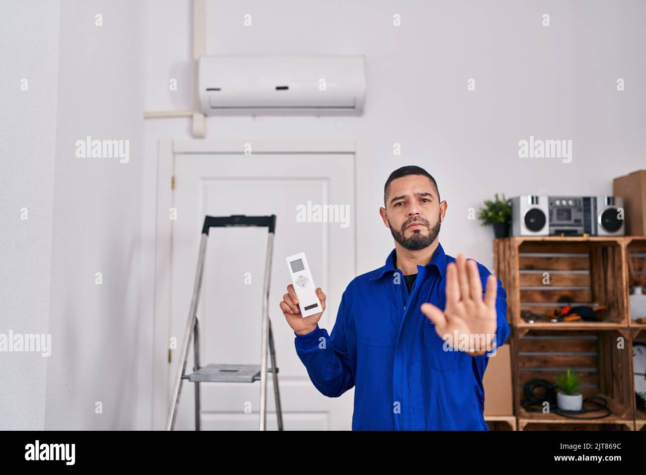 Un réparateur hispanique travaillant avec un climatiseur à main ouverte faisant signe d'arrêt avec une expression sérieuse et confiante, geste de défense Banque D'Images