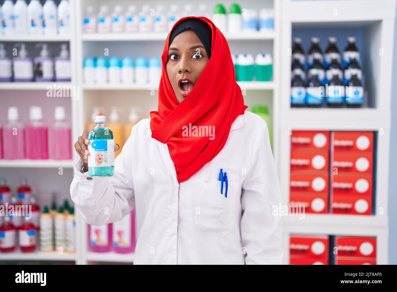 Jeune femme arabe travaillant à pharmacie drugstore holding sirop peur et stupéfait avec la bouche ouverte pour la surprise, le visage incrédulé Banque D'Images