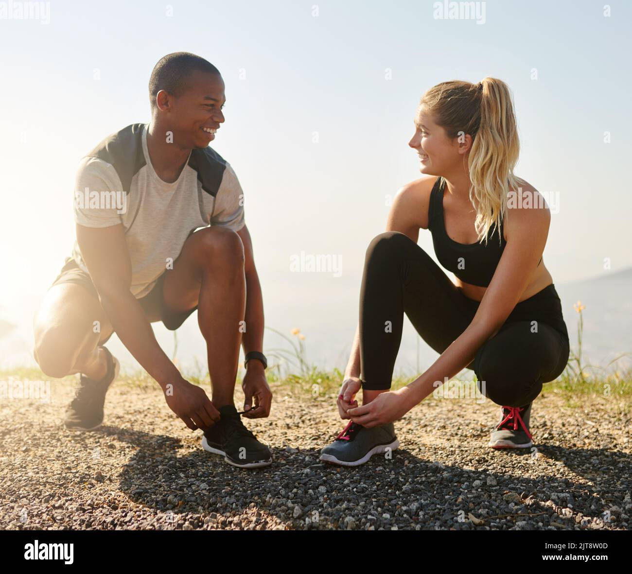 Ils partagent les mêmes objectifs de forme physique. Un jeune couple en forme de femme nouant leurs lacets avant une course à l'extérieur. Banque D'Images