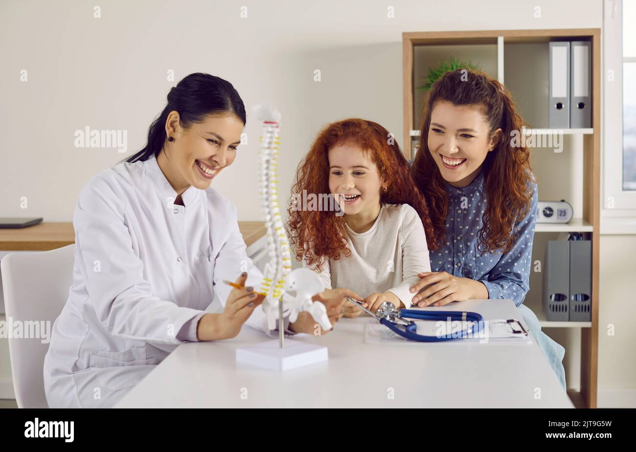 Joyeux médecin, parent et petit enfant regardant le modèle anatomique de colonne vertébrale et rire Banque D'Images