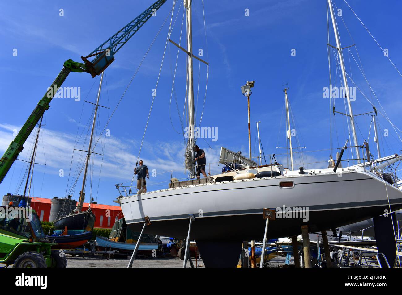 Grue levant un mât sur un bateau à voile se tenant dans le chantier de Llanion est, Llanion est, Pembrokeshire, pays de Galles Banque D'Images