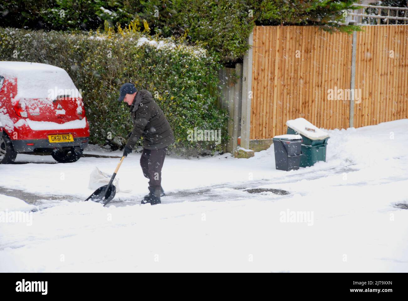 Homme qui pelle la neige de la route pour donner accès à la voiture malgré la neige qui tombe encore Banque D'Images