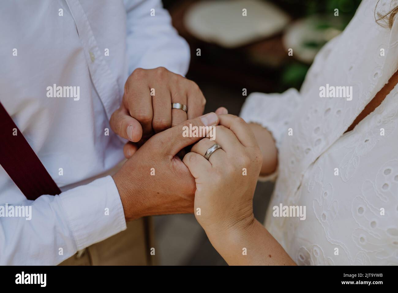 Gros plan de la mariée et du marié tenant les mains avec des anneaux de mariage à la réception à l'extérieur dans l'arrière-cour. Banque D'Images