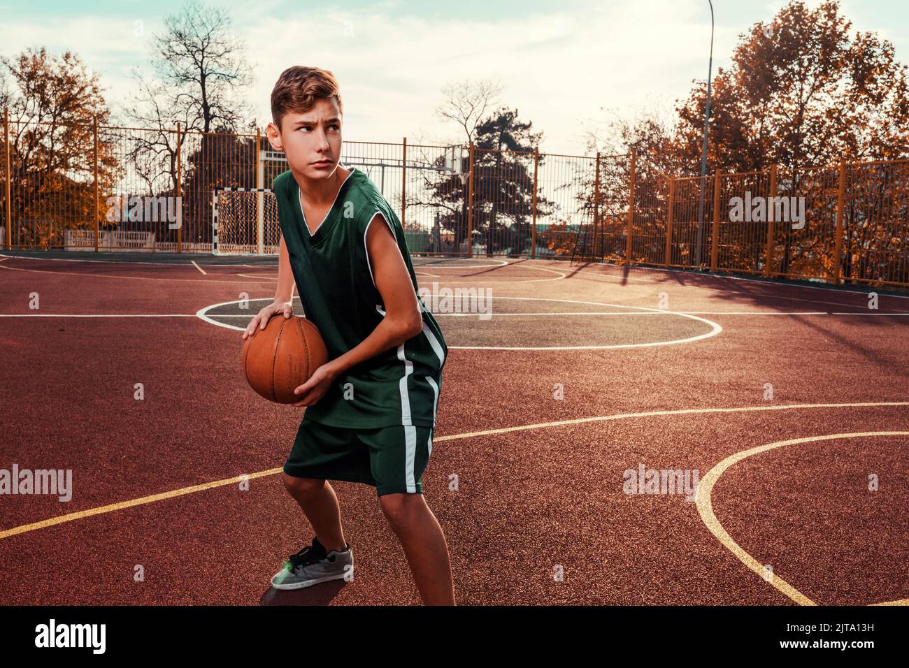 Sports et basket-ball. Un jeune adolescent dans un survêtement noir pose  avec un basket-ball dans ses mains et est prêt à lancer. En arrière-plan,  un basketba Photo Stock - Alamy