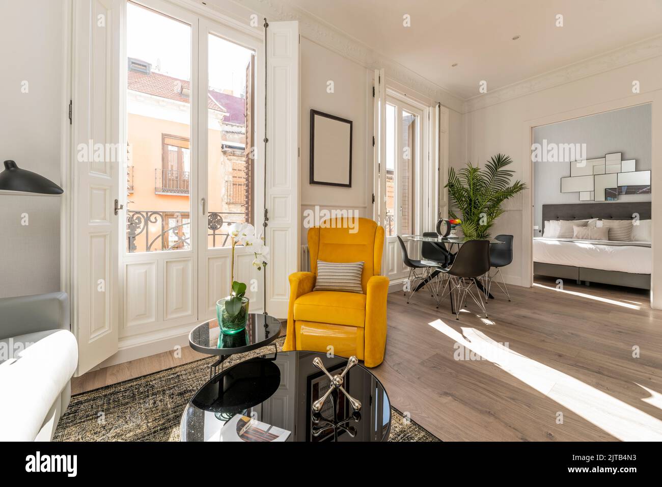 Séjour d'une maison avec tapis, un causeuse en tissu gris avec une table latérale avec des plantes, plusieurs balcons avec fenêtres et volets en bois blanc an Banque D'Images