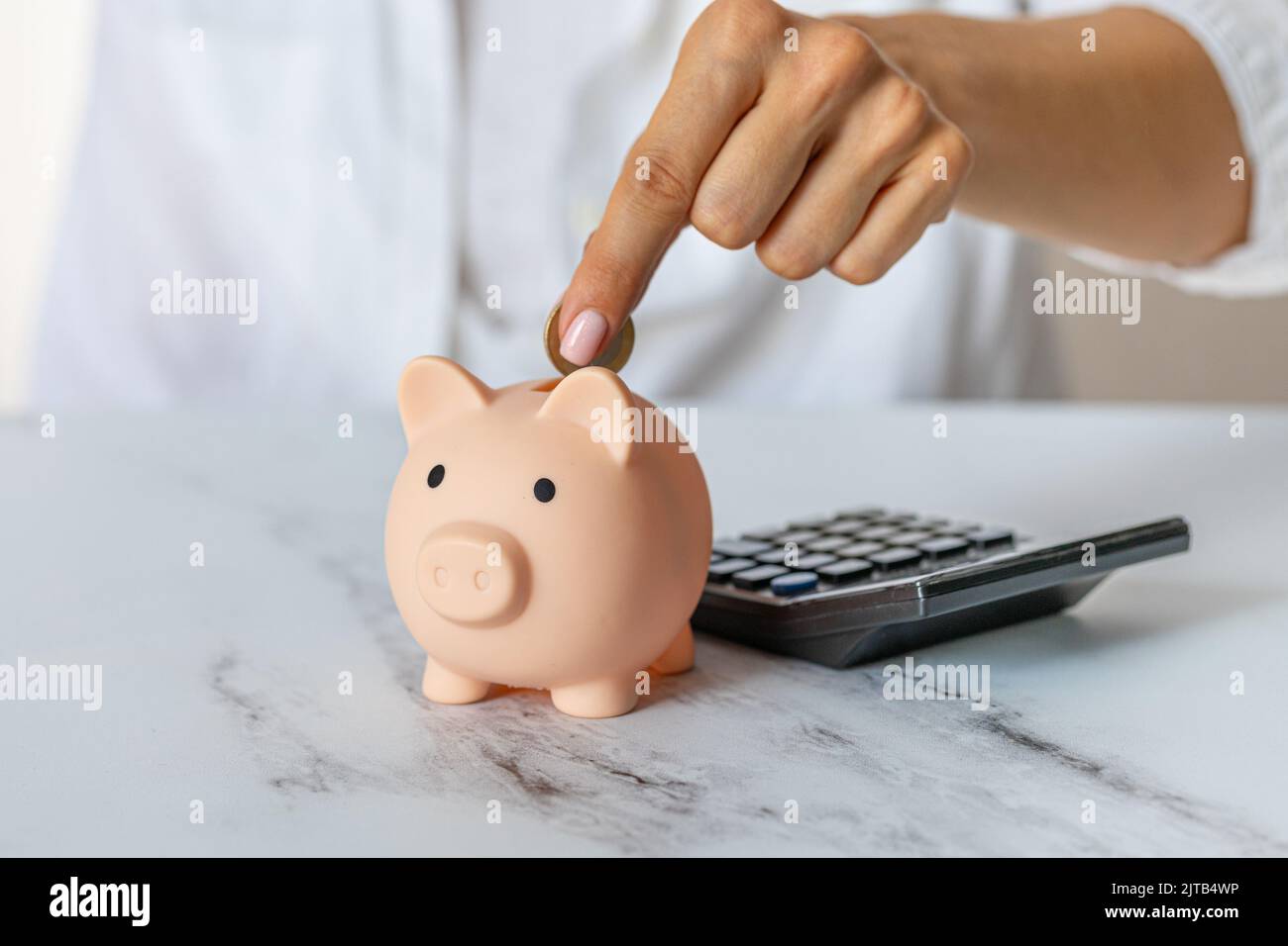 Gros plan des mains d'une femme mettre une pièce d'euro dans une banque de piggy, à côté d'une calculatrice sur la table.investissement correct. Économiser de l'argent en temps de crise et Banque D'Images