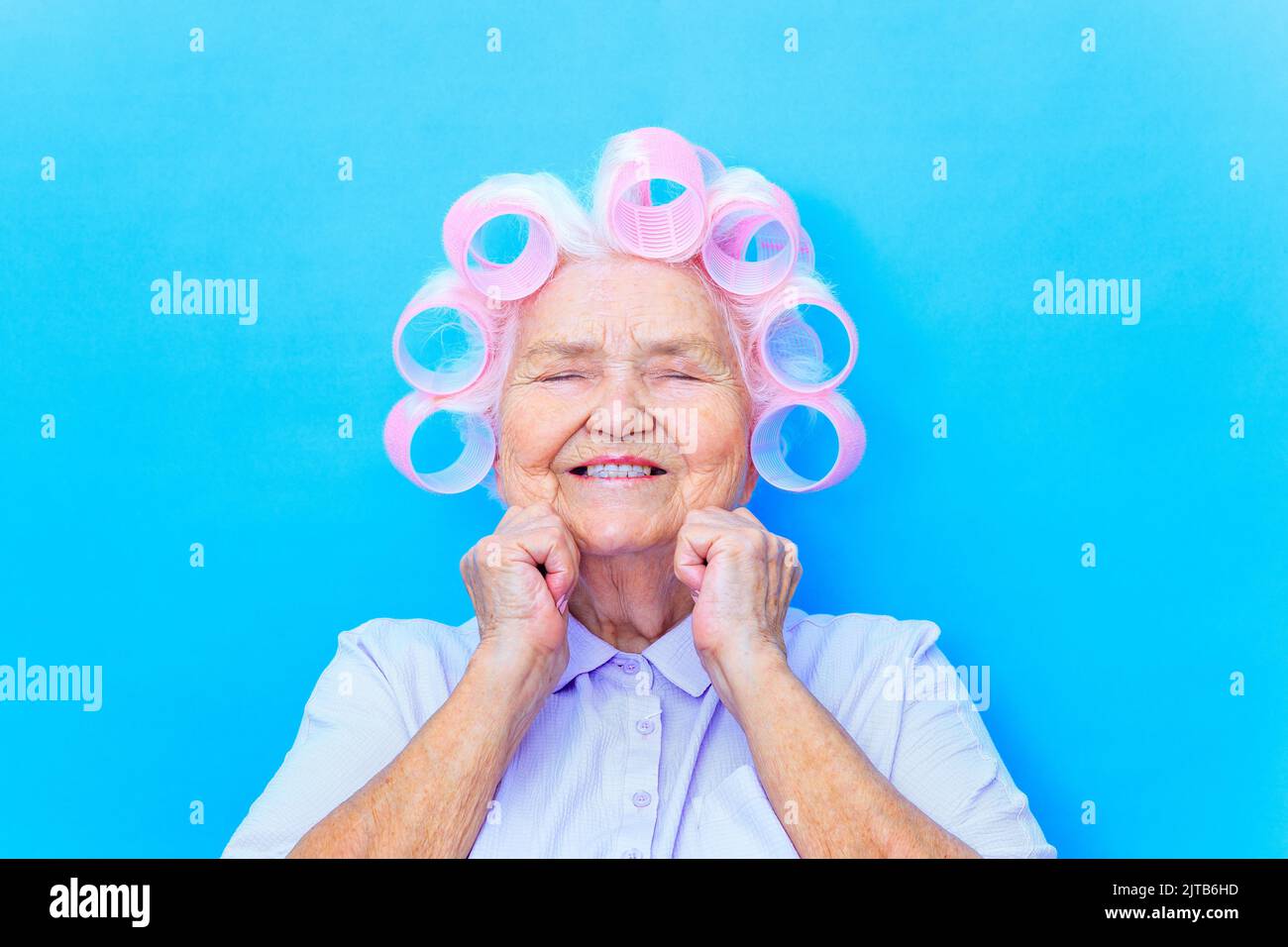 Charmante vieille femme avec des curlers sur blanc gris cheveux porter chemise se préparer pour la date isolé sur fond bleu de brigth Banque D'Images