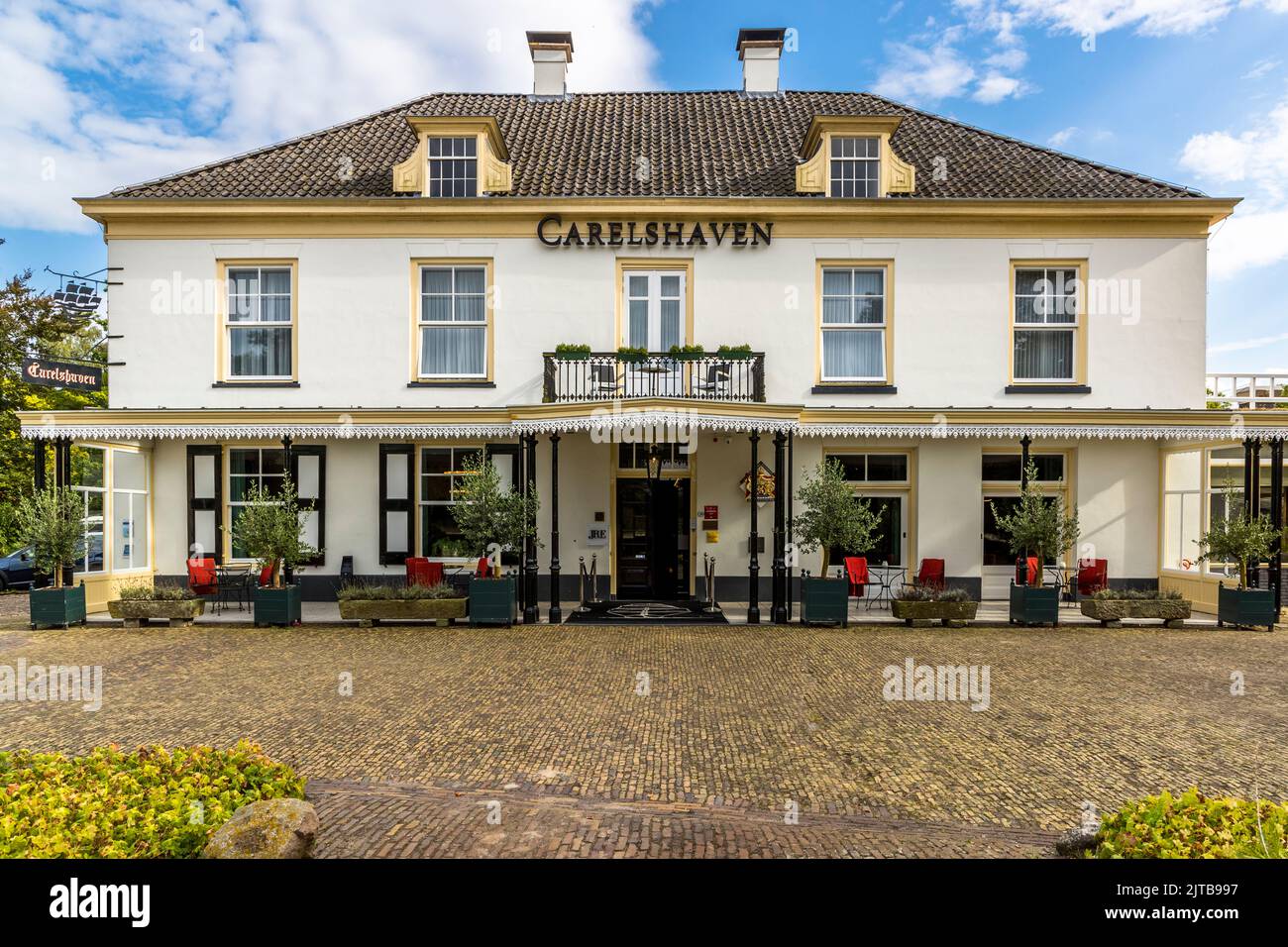 L'hôtel et restaurant Carelshaven à Delden, commune de Hof van Twente, aux Pays-Bas, existe depuis 1772 et est nommé d'après Graaf Carel George van Wassenaer Obdam, qui a également fait construire le canal Twickelervaart. La cuisine de l'établissement a détenu une étoile Michelin de 1972 à 1986. Des fauteuils rouges sont prêts sous la façade blanche aux cadres de fenêtres jaunes. Banque D'Images