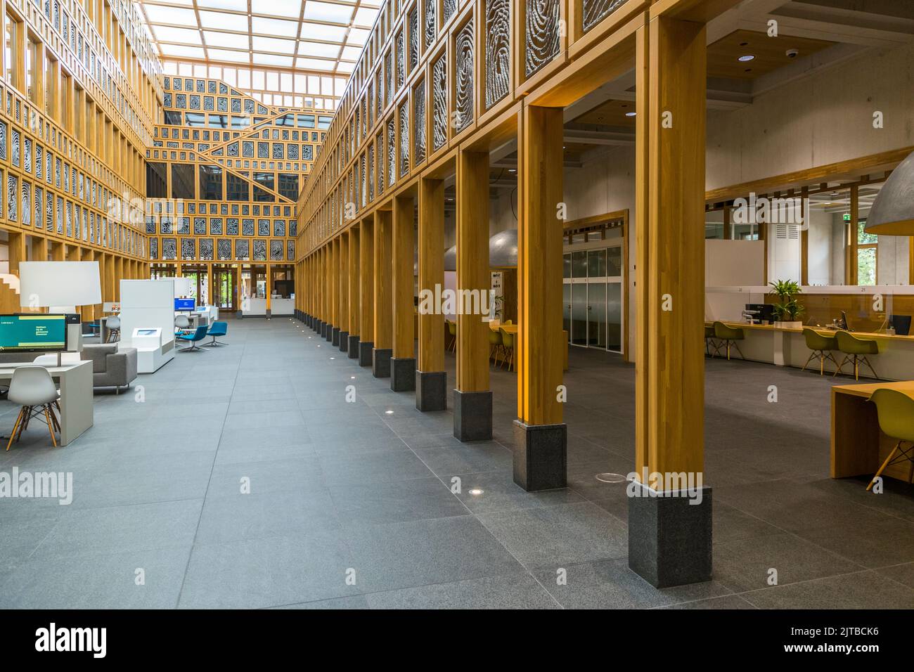 Le Stadhuiskwartier à Deventer, l'une des neuf villes hanséatiques historiques sur la rivière IJssel, province d'Overijssel, Pays-Bas, est l'extension de l'hôtel de ville achevée en 2016 par les architectes Neutelings Riedijk. Sa façade en verre encadrée de jaune porte l'œuvre d'art „Deventer Raamwerk“ (Cadre de Deventer) de l'artiste Loes ten Anscher : 2 264 empreintes digitales de résidents de Deventer moulées en aluminium, chaque cassette en verre peint montrant une empreinte digitale unique. À l'intérieur, un passage court entre des colonnes de support en bois, avec des meubles de salon à gauche et des postes de travail alignés le long d'un long comptoir à droite. Banque D'Images