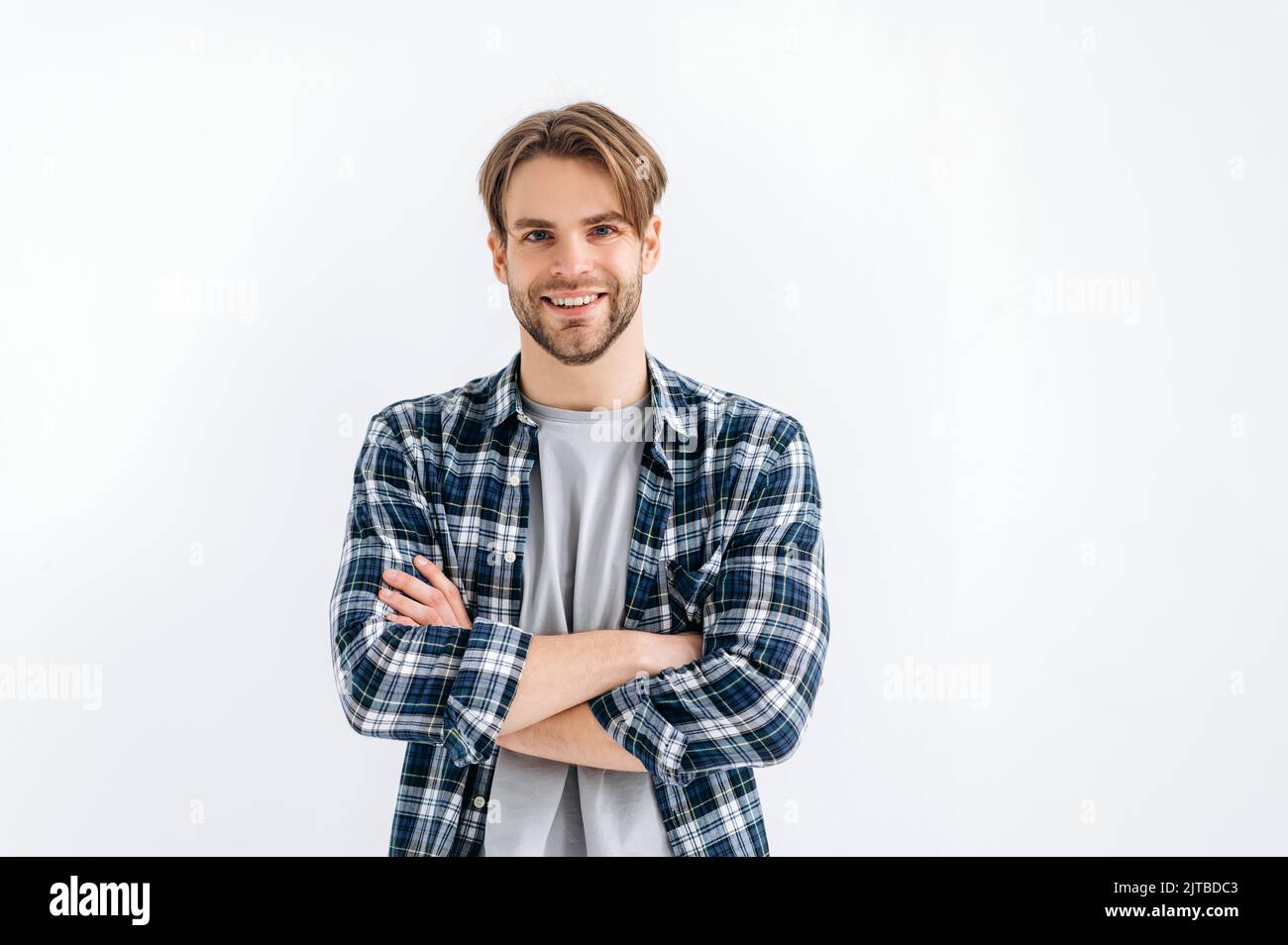 Portrait d'un homme de style caucasien positif et confiant aux yeux bleus, debout sur un fond blanc isolé avec des bras croisés, regardant l'appareil photo, souriant amical Banque D'Images