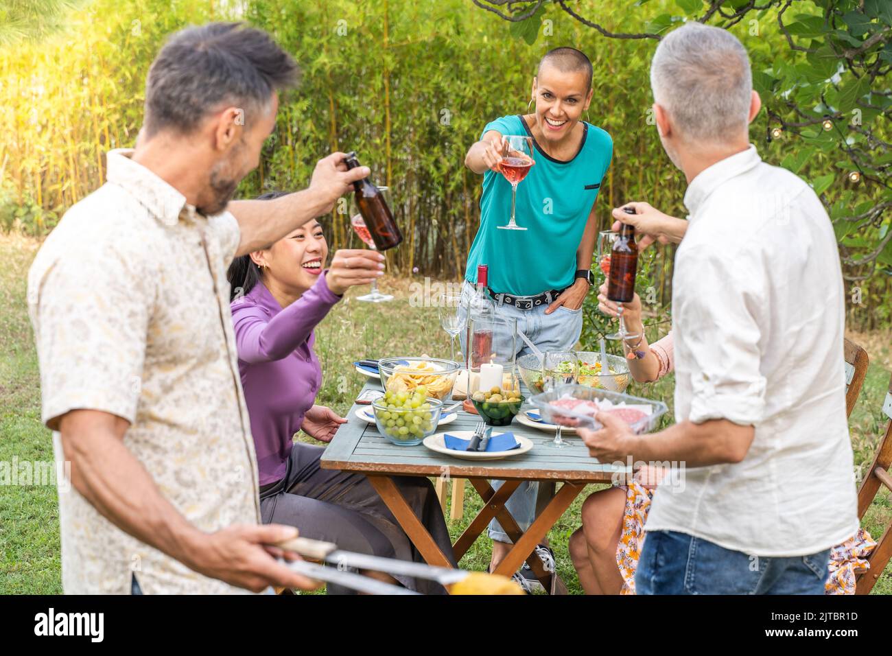 Des amis heureux en train de griller avec un grand sourire autour de la table souriant les gens qui mangent au barbecue sur le patio de la maison. Concept de gaieté. Banque D'Images