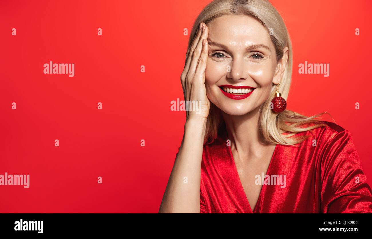 Belle et élégante femme mûre avec cheveux blonds, peau claire et brillante du visage, portant robe rouge et rouge à lèvres pour la fête de noël, nouvel an, concept Banque D'Images