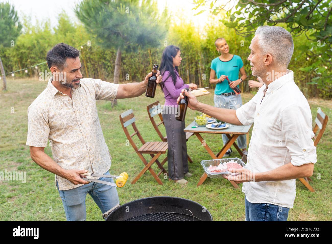 Des amis heureux qui rient et grillent avec un grand sourire autour du barbecue. Souriant, les gens mangent sur le patio de la maison en été. Concept de joie. Banque D'Images