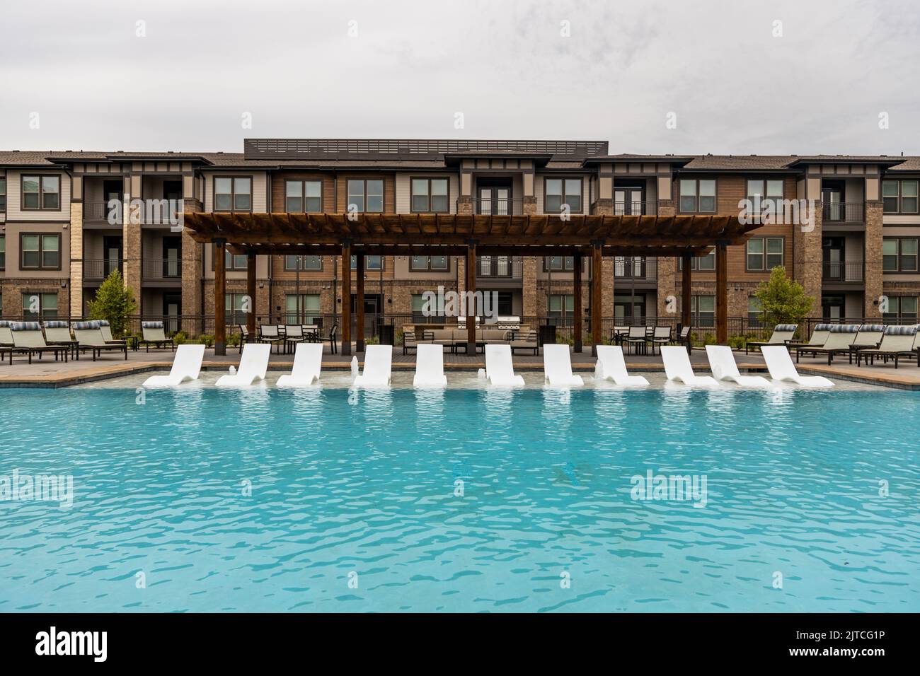 Espace de loisirs avec piscine et chaises longues dans un complexe résidentiel ou un hôtel moderne, zone de repos dans le complexe avec bâtiment marron sur fond Banque D'Images