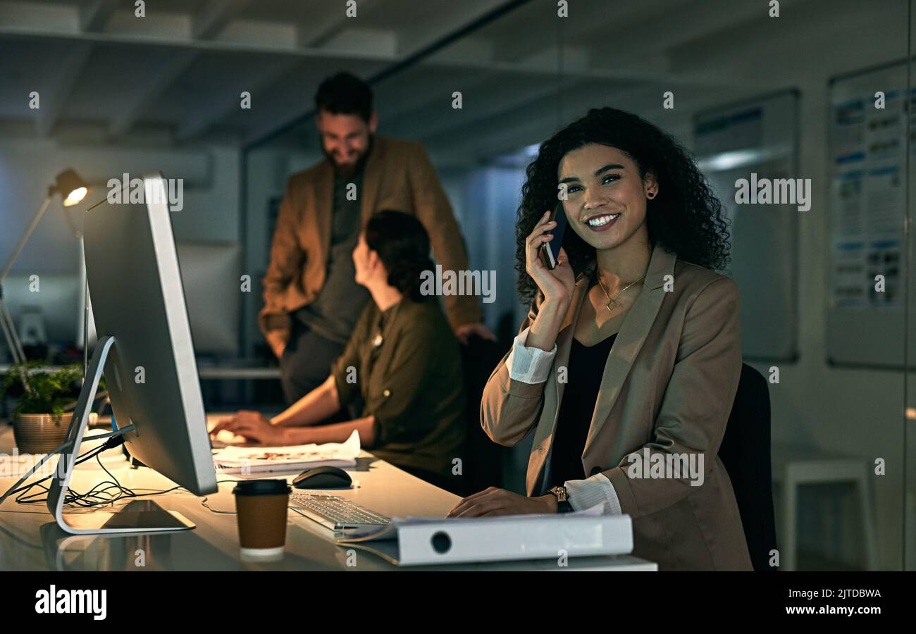 Elle n'a aucun problème pour mettre du temps supplémentaire pour les clients. Une jeune femme parlant au téléphone avec ses collègues en arrière-plan. Banque D'Images