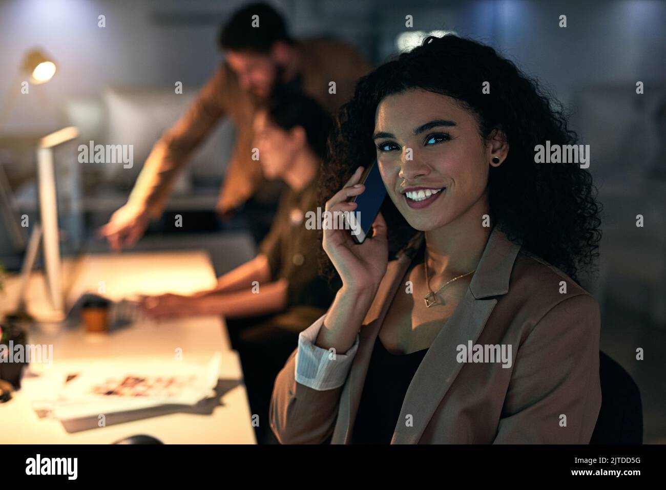 Une jeune femme qui parle au téléphone avec ses collègues en arrière-plan va faire le maximum pour ses clients. Banque D'Images