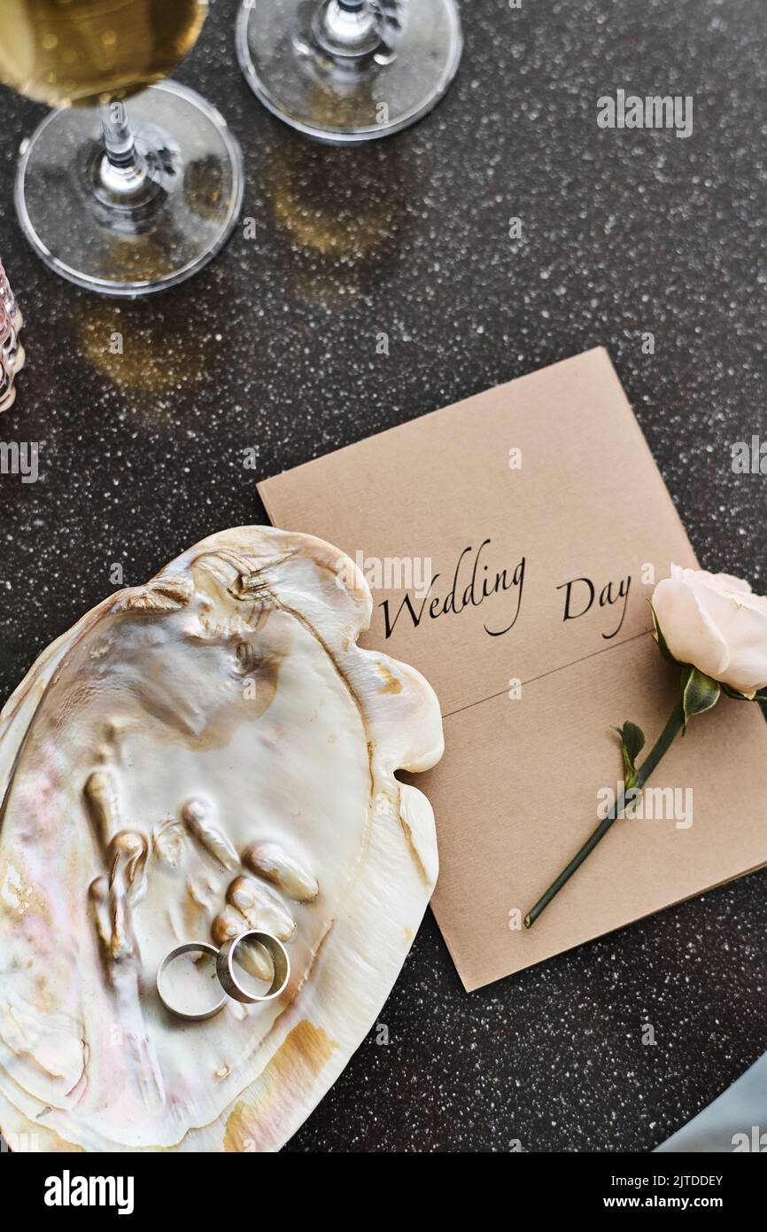 Flatlay de composition de mariage de coquillages de perle avec deux anneaux, invitation, rose blanc frais et flûtes avec champagne sur la table Banque D'Images