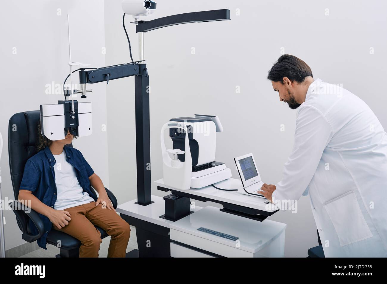 Optométriste effectuant un test de vision pour un enfant mâle à l'aide d'un phoroptère moderne à la clinique d'ophtalmologie. Examen des yeux et diagnostic de la vision chez les enfants Banque D'Images