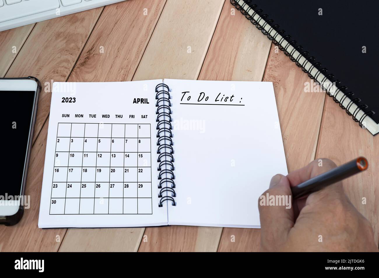 Mains avec stylo écrire à la liste des tâches avec le calendrier d'avril 2023 sur le carnet. Banque D'Images