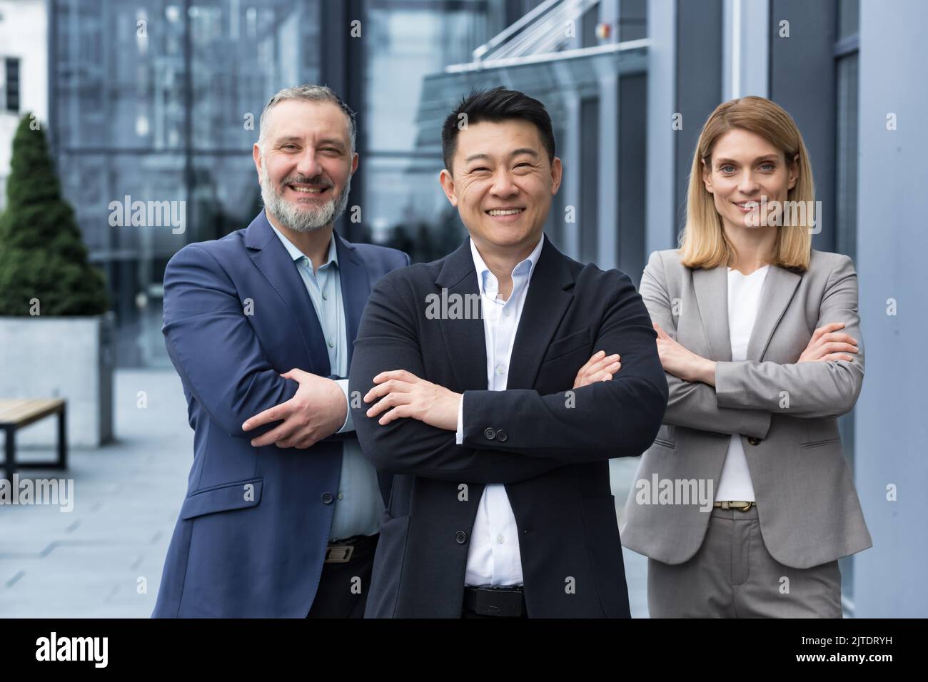 Équipe d'affaires diversifiée réussie, trois employés souriant et regardant la caméra, équipe de rêve avec un patron asiatique à l'extérieur du bâtiment de bureau, des collègues dans des costumes d'affaires Banque D'Images