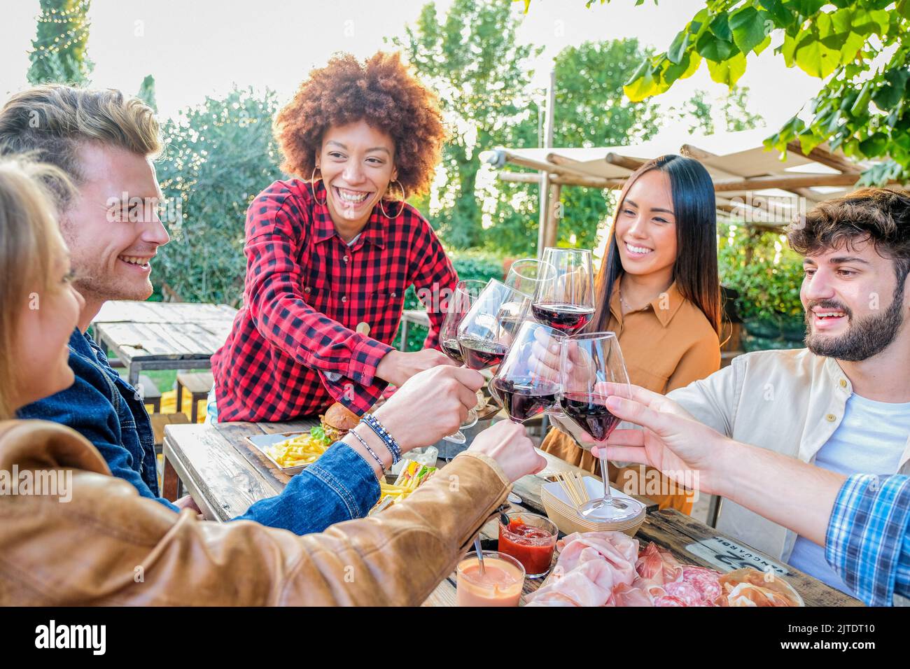 Groupe d'amis multiraciaux prenant des selfies et célébrant avec des verres à vin à l'heure du dîner en terrasse - les jeunes mangent et boivent du vin rouge à Banque D'Images
