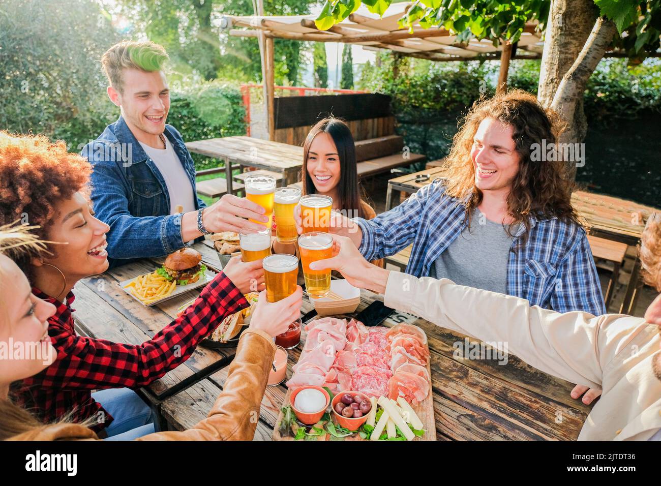 Groupe d'amis multiethniques vivant un style de vie sain et souriant et plaisantant tout en buvant de la bière au restaurant de pub extérieur - les jeunes se régalent avec humour Banque D'Images