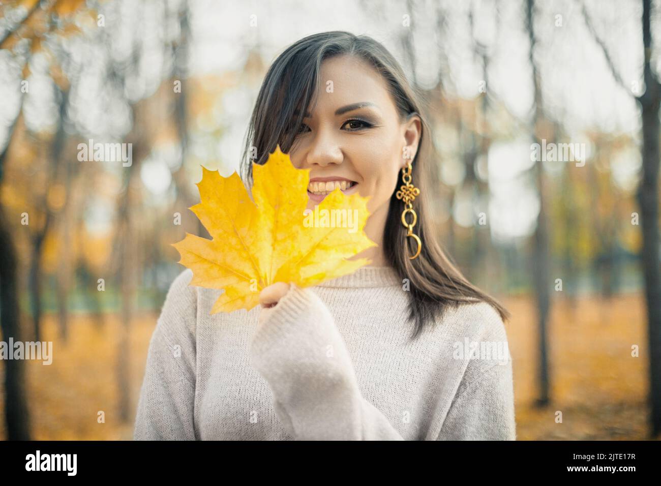 Jeune femme souriante dans un chandail gris avec une feuille d'érable jaune d'automne dans sa main. Ambiance d'automne Banque D'Images