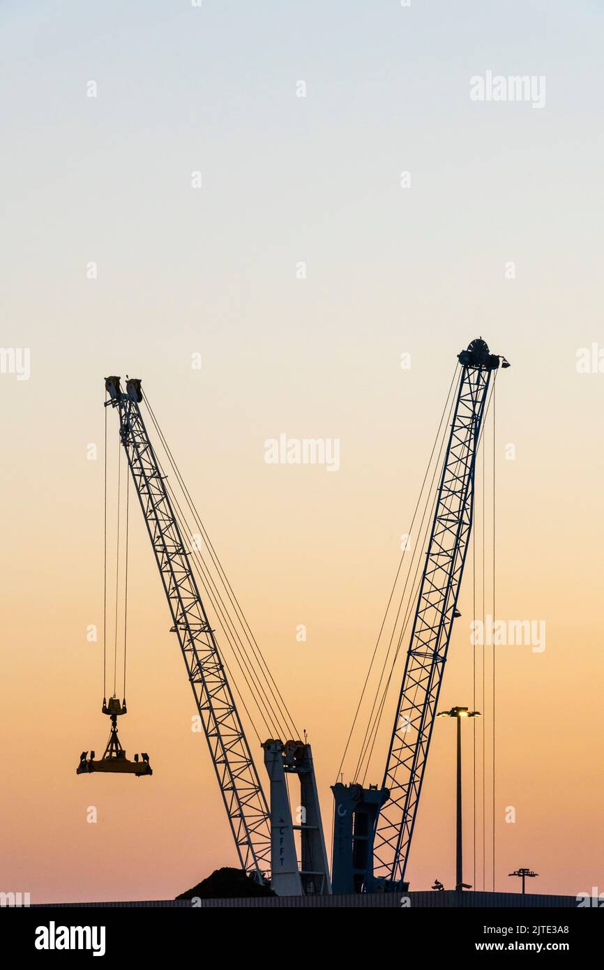 Grues de chantier silhouetées contre le coucher du soleil, dans le port de Civitavecchia, Italie Banque D'Images
