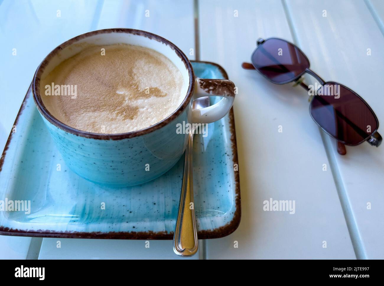 Cappuccino café dans une tasse moderne bleue et soucoupe avec une paire de lunettes de soleil Banque D'Images