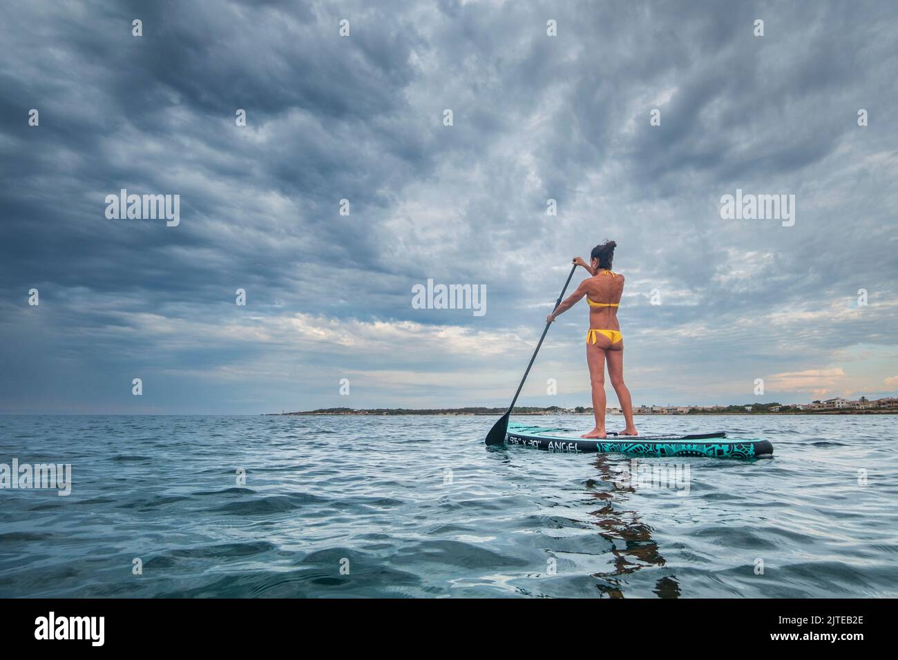 Femme pagayant sur une planche de surf sous un ciel spectaculaire, sa Rapita, Majorque, Iles Baléares, Espagne Banque D'Images