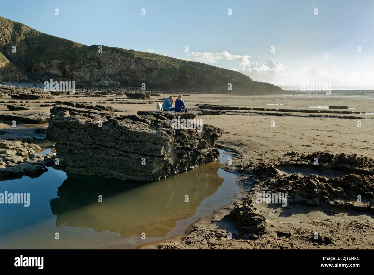 Les gens se reposant sur des roches calcaires sur la plage de Southerndown avec leur chien, Dunraven Bay à marée basse, Glamourgan Heritage Coast, South Wales, Royaume-Uni, octobre. Banque D'Images