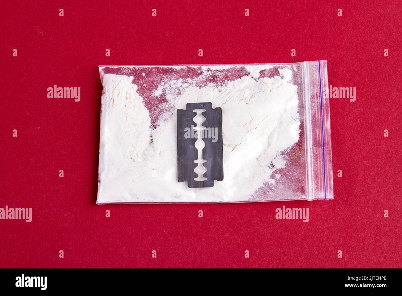 Rasoir et paquet de poudre de cocaïne pour ronfler isolé sur le rouge. Vue de dessus en gros plan. Banque D'Images
