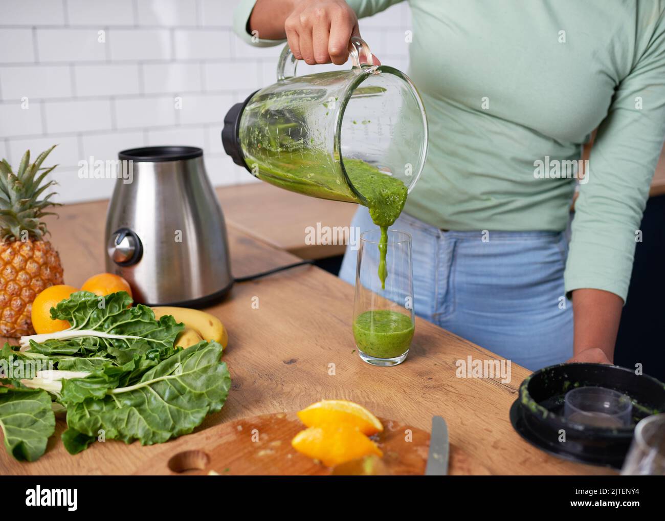 Gros plan sur une femme qui verse du smoothie vert maison dans un verre Banque D'Images
