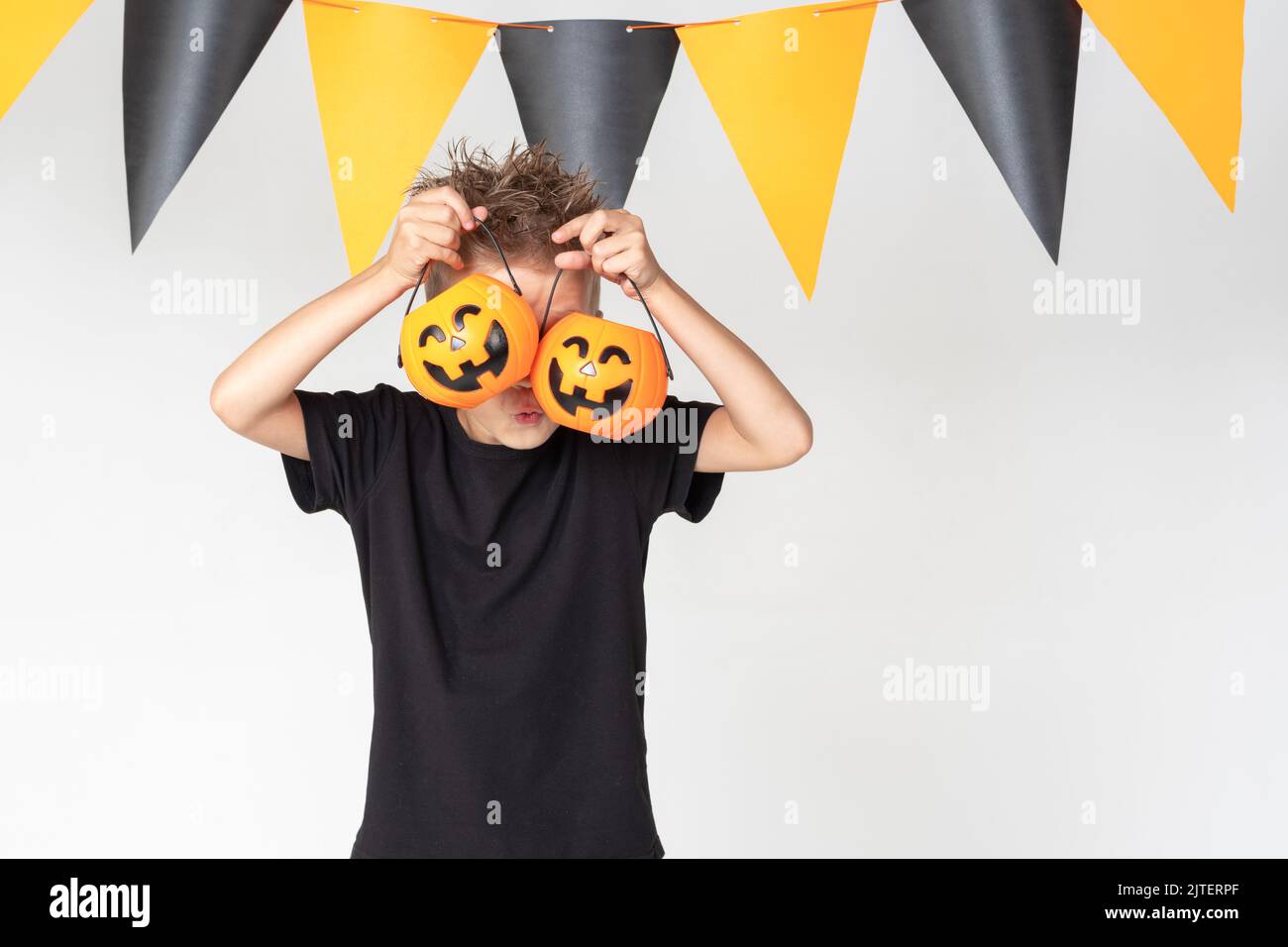 Halloween pour enfants. Un beau garçon émotif dans un t-shirt noir tient la lanterne de Jack sur un fond blanc studio décoré d'un noir et d'orange Banque D'Images