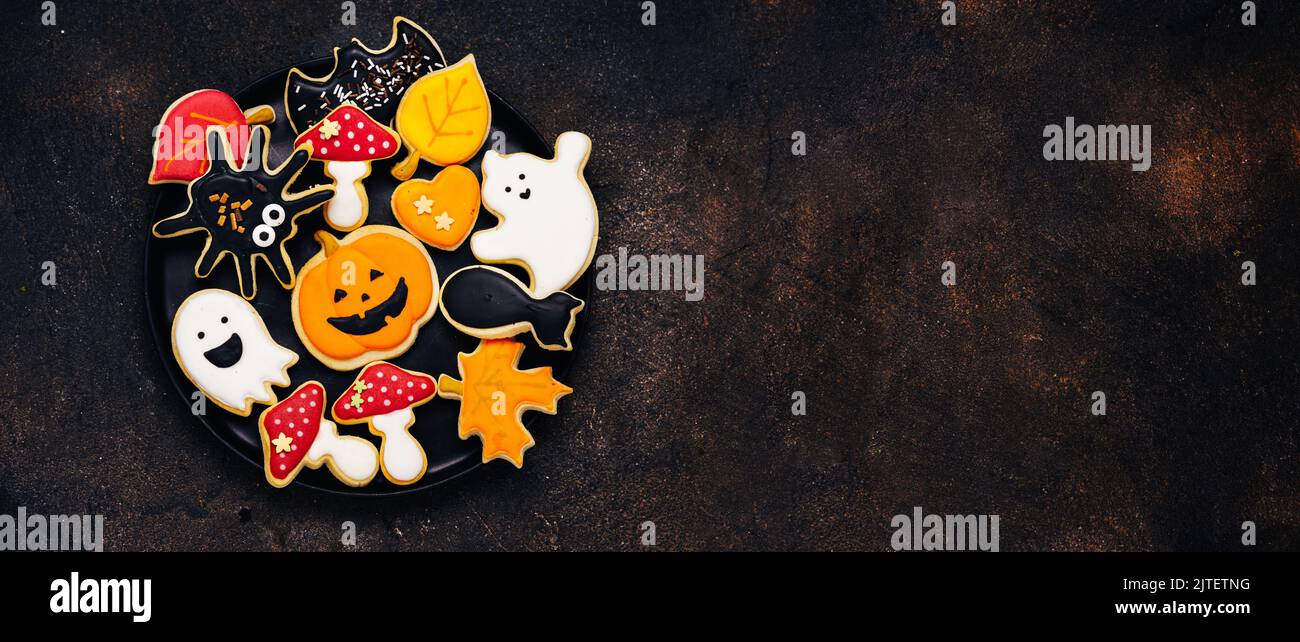 Biscuits au sucre d'Halloween avec glase sur fond marron foncé - citrouille, champignons, chat noir, fantômes, araignée, batte. Longue bannière avec espace de copie Banque D'Images