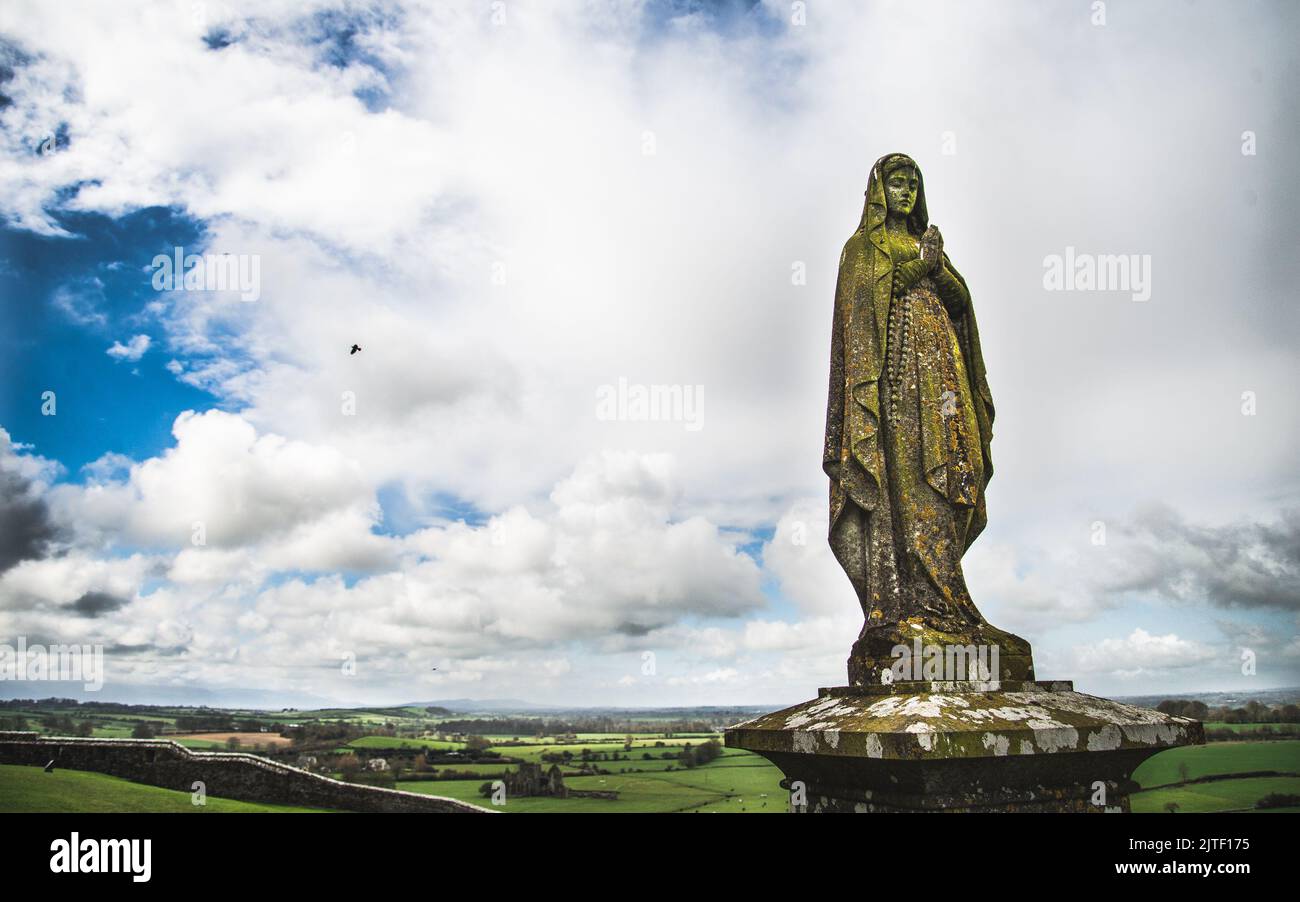 Ancienne statue de Marie sur un pilier avec ciel et campagne irlandaise en arrière-plan. Banque D'Images