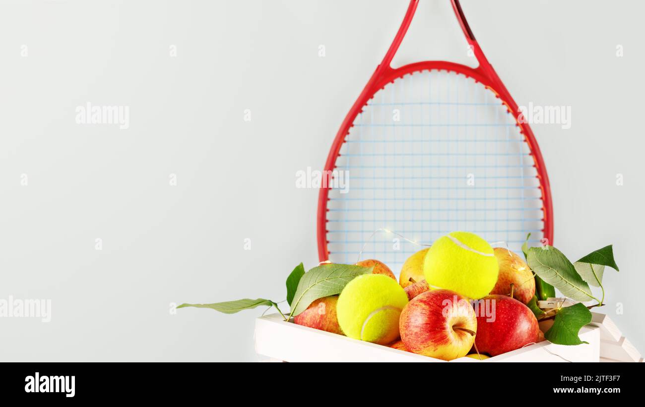 Composition de tennis avec balles de tennis jaunes, pommes dans une boîte en bois blanc et raquette de tennis rouge sur fond bleu avec espace de copie. Concept de Healt Banque D'Images