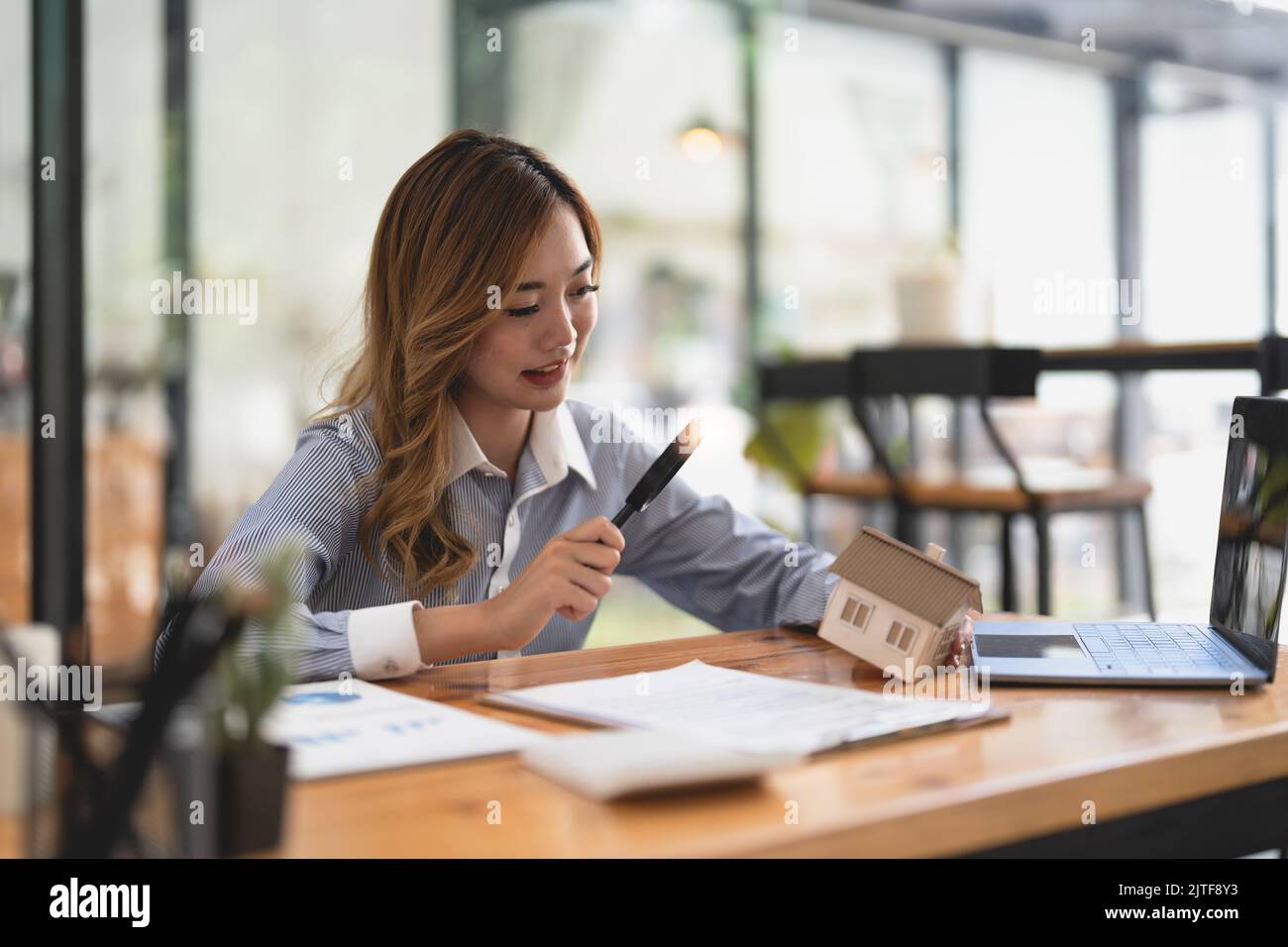 Recherche d'agence immobilière, d'assurance de biens, de prêt hypothécaire ou de maison neuve. Femme avec loupe sur une maison en bois à son bureau Banque D'Images