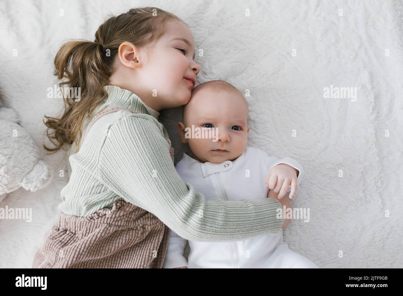 Fille (2-3) embrassant nouveau-né (0-1 mois) frère sur le lit Banque D'Images