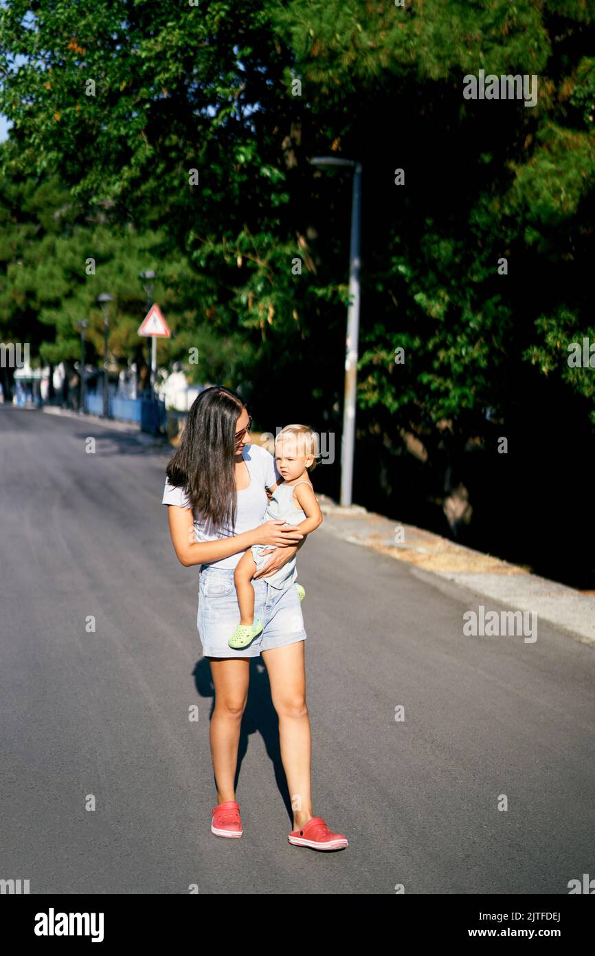 Budva, Monténégro - 12.07.22: Maman porte une petite fille dans ses bras marchant le long de la route Banque D'Images