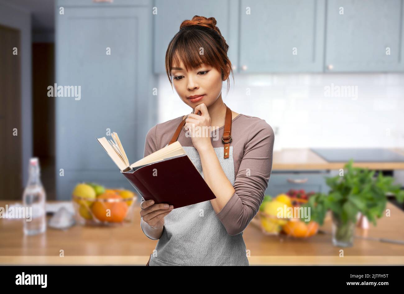 femme en tablier lisant le livre de cuisine à la cuisine Banque D'Images