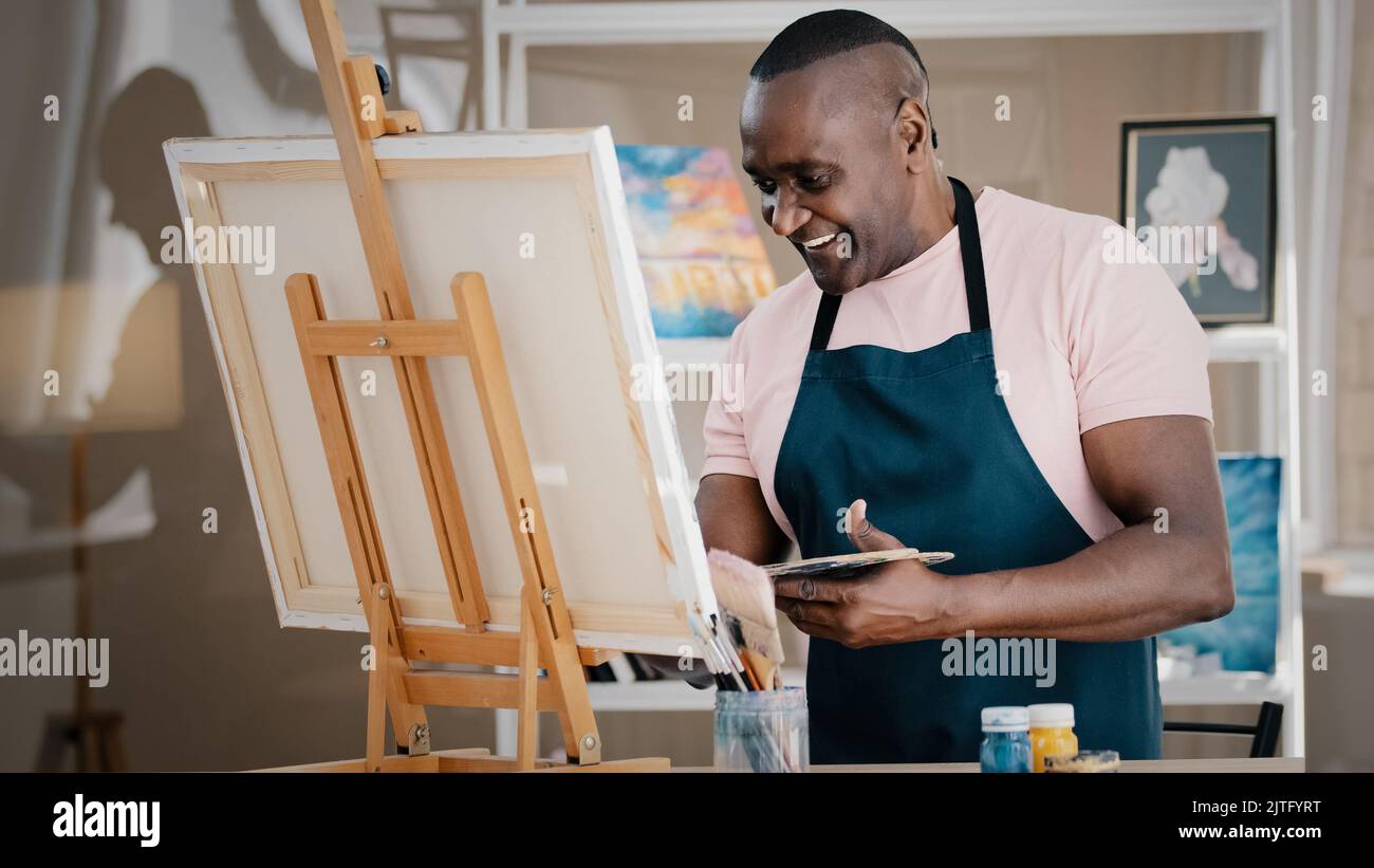 Vue latérale Happy sourire gai créatif talentueux inspiré ancien Africain américain senior artiste peintre masculin en tablier dessin tableau photo Banque D'Images