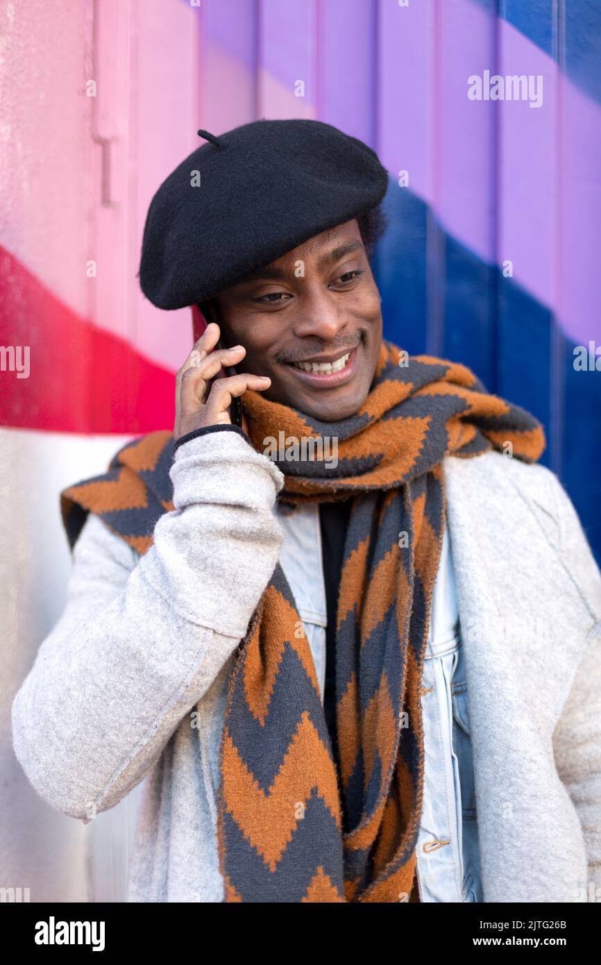 Portrait d'un jeune adulte afro-américain souriant parlant au téléphone. Il est isolé sur un mur multicolore. Banque D'Images