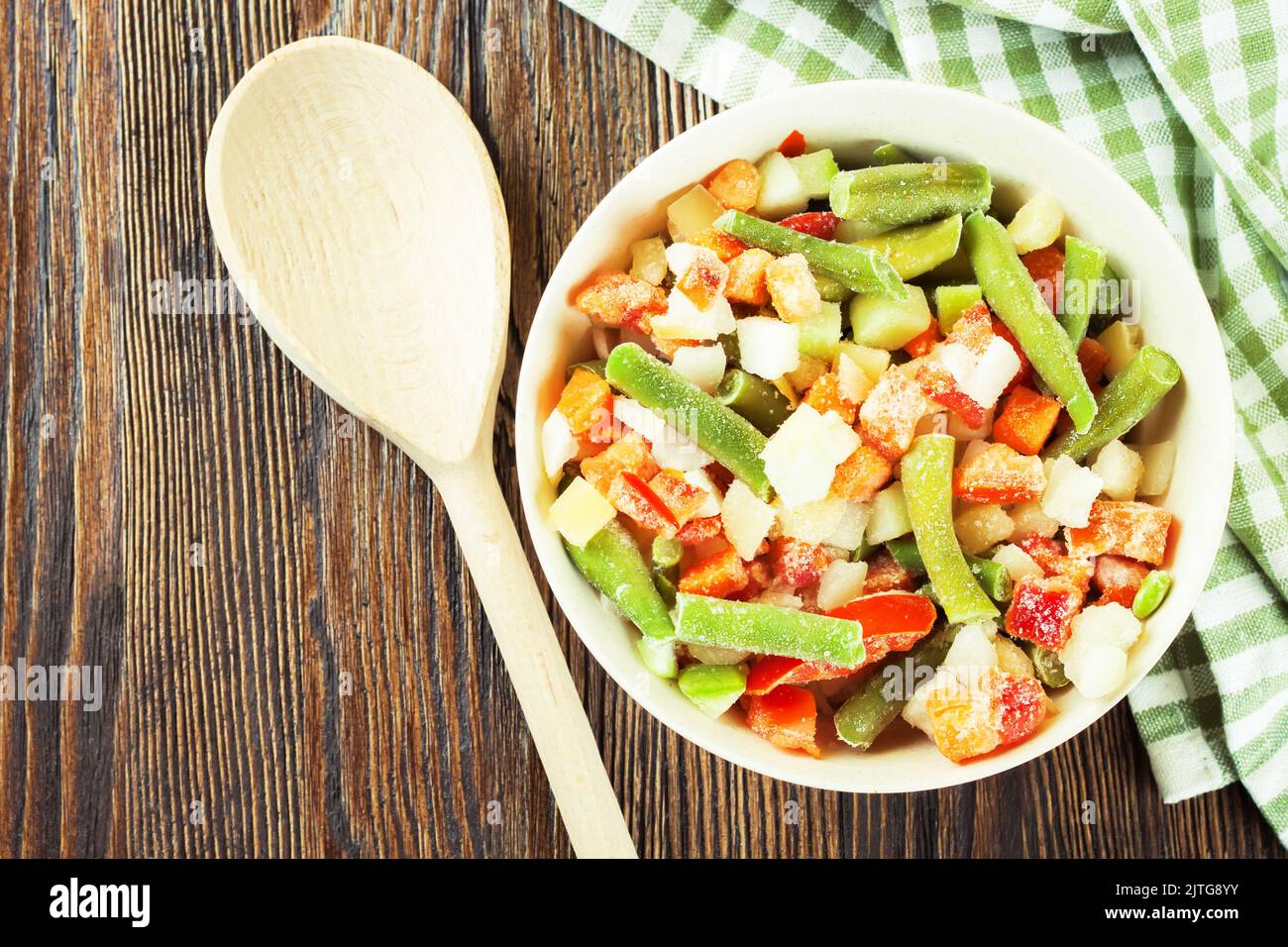 Un mélange de légumes surgelés assortis dans un bol blanc prêt à cuire sur une table en bois brun. Flat lay, vue de dessus avec espace de copie pour le texte Banque D'Images